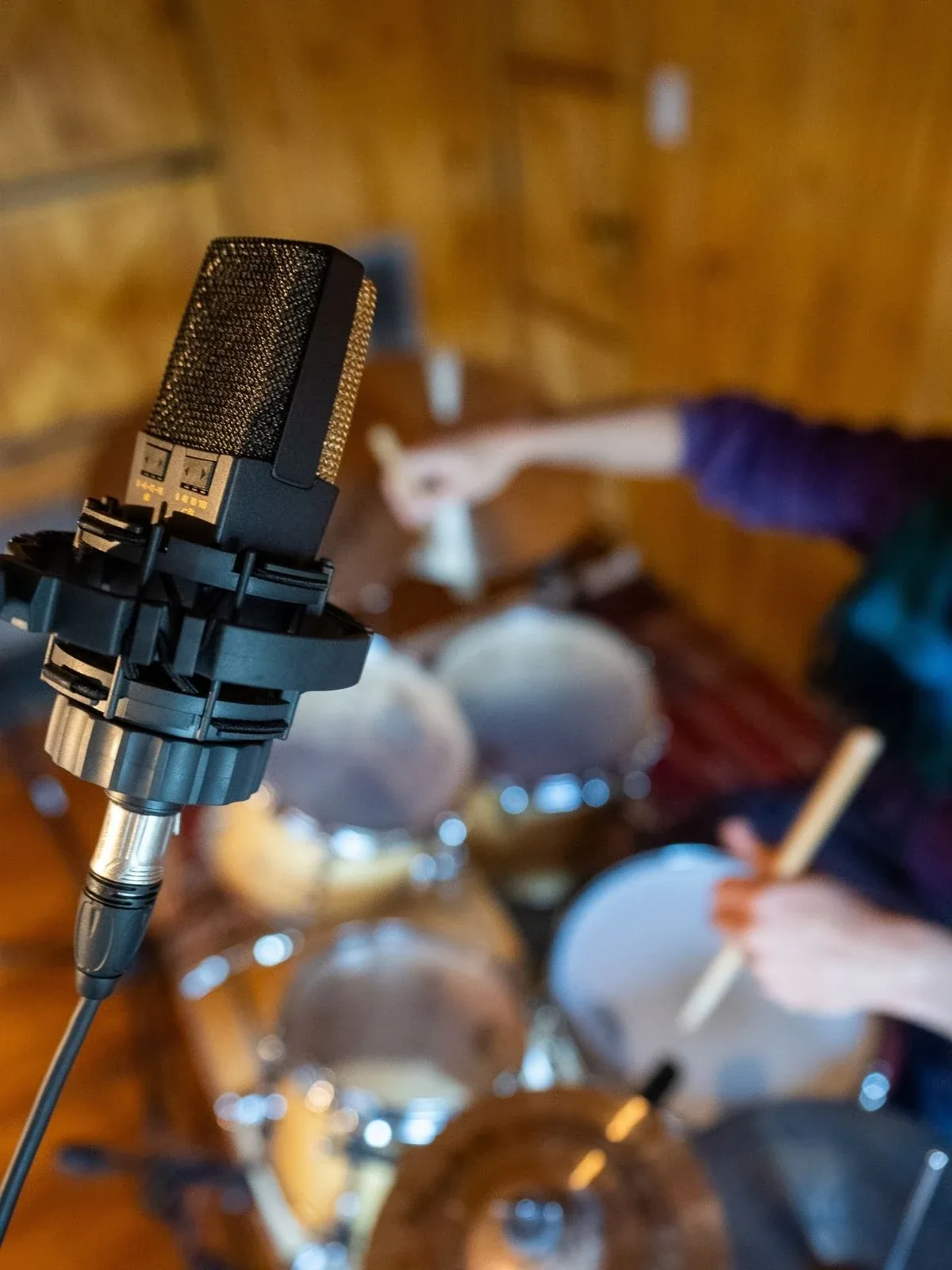 Micrófono condensador en primer plano, baterista tocando al fondo